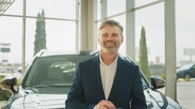 Orta yaşlı, olgun, yakışıklı, sakallı, takım elbiseli, beyaz saçlı bir adamın portresi. Arabasına yaslanmış ve almalı mı diye düşünüyor. Otomobil galerisinde yeni arabanın yanında duran müşteri