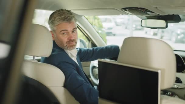 現代の新しい車の中で男を運転 後ろの景色 車のショールームでミラーのビジネスマンの反射 新しい車の中で正式な摩耗を身に着けている幸せな45秒の男は カメラを見て笑って振り向く — ストック動画