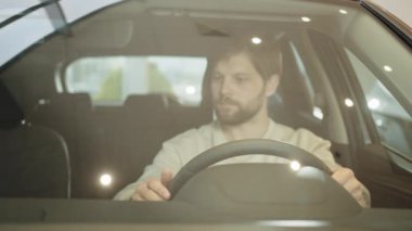 Erkek alıcı yeni bir arabada oturur ve kontak anahtarını takar, arabayı çalıştırır. Genç adam yeni bir arabanın direksiyonunu tutuyor, yeni bir alımdan memnun. Yeni bir araba alıyorum. Dikey görünüm