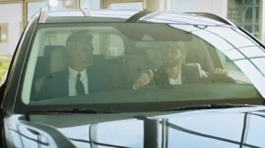 Galeride yeni aldığı arabada oturan neşeli adam, perakende işi otomotiv satan profesyonel bir pazarlamacıdan araba anahtarı alıyor ve kiralama hizmeti veriyor.