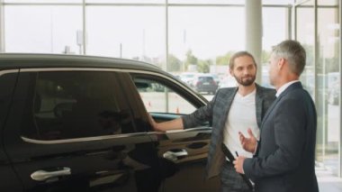 Müşterisi olan bir erkek satıcı, elinde yeni bir tablet sergi salonunda duran belgeler taşıyor. Orta yaşlı bir işadamı araba galerisinde genç ve yakışıklı bir adama araba satıyor.