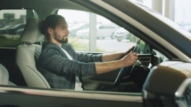 Kendine güvenen yakışıklı adam galeriden yeni bir araba alıyor. Resmi giyinmiş saygıdeğer mutlu iş adamı yeni alınmış bir elbisenin içinde oturuyor. Araba galerisinde tüketici. İş adamı araba seçiyor..