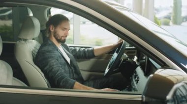 Yeni arabanın içinde oturan mutlu beyaz adam ve galeride yeni modelin tüm fonksiyonlarını kontrol ediyor. Modern kuaförde çeşitli otomobilleri inceleyen erkek müşteri. Modern galeride arabayı inceleyen adam..