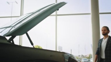 Başarılı bir erkek müşteri siyah otomobilin kaputunu açıyor. Genç adam yeni arabaya bakıyor. Araba galerisinde tüketici. İş adamı araba kuaförünü seçiyor.