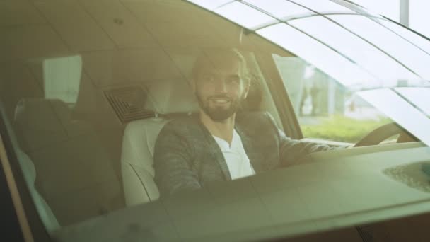 正の白人男性高級車の運転席に座って カメラに笑みを浮かべて ハンドルに手を握って 購入前に車両の検査 サロンで車を調べる男 — ストック動画