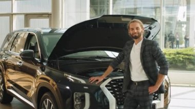 Araba galerisinde tüketici. Satıcıdan araba seçen yakışıklı işadamı, satış mağazasında yeni bir arabaya karşı duran otomobil erkek müşterisinin motorunu inceliyor..