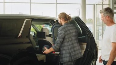 Orta yaşlı gri saçlı bir adam ve yetişkin oğlu araba galerisinde yeni bebek koltuğu deniyorlar. Bir galeride iki yaşlı baba ve yetişkin oğul yeni bir araba seçiyor. Adam otomatiği seçer. Satış konsepti.