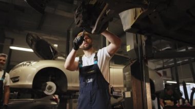 Deneyimli bir tamirci LED lamba kullanarak asansörde aracın altına bakıyor. Otomobil servisinde iki araba tamircisi teşhis etti. Bir araba atölyesinde çalışma