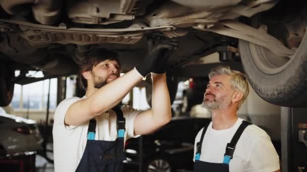 Dwóch Pewny Siebie Zawodowych Mężczyzn Mechanik Samochodowy Badający Zawieszenie Samochodu — Wideo stockowe