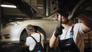 Tamirci araba servisinde çalışıyor. Otomobil servisinde iki araba tamircisi teşhis etti. Bir araba atölyesinde çalışma. Araba tamirhanesinde araba tamiri. Araba servisi, onarım, bakım.