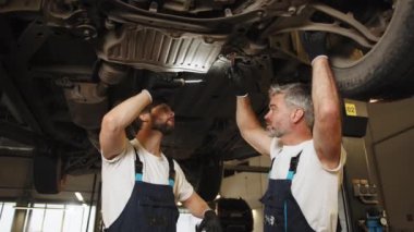 İki beyaz tamirci, otomobil motoru servisinde çalışıyor. Otomotiv bakım ve onarım işleri yapan bir teknisyen. Profesyonel tamirci. Atölye servis istasyonu.
