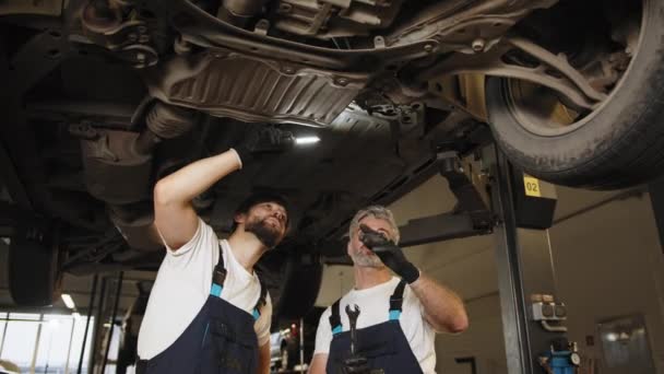 Двоє Впевнених Професійних Чоловіків Які Вивчають Механіку Автомобіля Підвішують Підйомний — стокове відео