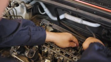 Genç oto tamircisi, karşıdaki motoru teşhis için söker ve atölyedeki standda tamir eder. Otomobil tamircisi garajda çalışıyor. Tamir servisi. Tanınmayan tamircinin ellerini kapat