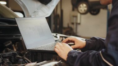 Kendine güvenen yetenekli bir oto elektrikçi, bilgisayar bilgisayarı kullanarak araba motorlarının tamir ve onarım parçalarını kontrol ediyor. Tamirci otomobil tamiri için bir motor tamir ediyor.