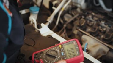Man using multimeter to measure the voltage of the batteries. Mechanic doing car inspection, he is testing car battery with tester. Check battery voltage with electric multimeter