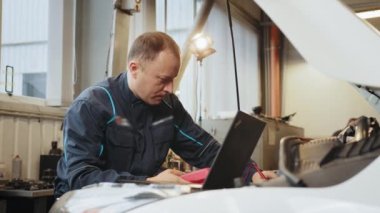 Profesyonel araba tamircisi elektrikçi voltaj multimetresi kullanıyor, oto tamir servisinde çalışıyor. Düzenli önleyici araba bakımı. Otomobil servisi, bakım konsepti. Bir araba girişinde sorun var.
