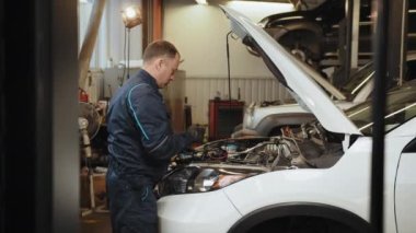 Otomobil servisi, bakım konsepti. Tamirci arabayı kontrol ediyor, benzin istasyonunda dizüstü bilgisayarla tarama yapıyor. Endüstriyel servisden motor tamirine. OBD Yönetim Kurulu Teşhisi.