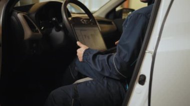 Otomobil servisi, bakım konsepti. Dizüstü bilgisayarı olan tamirci otomobil servisinde araba kontrolü yapıyor. Tamirci arabayı kontrol ediyor, benzin istasyonunda dizüstü bilgisayarla tarama yapıyor. Bilgisayar kullanan bir adam