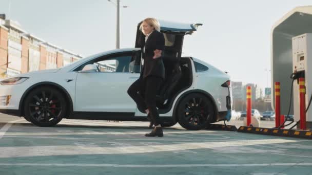 현대의 친환경 시간을 즐기는 자동차 비즈니스 슈트를 여성이 역에서 자동차를 — 비디오