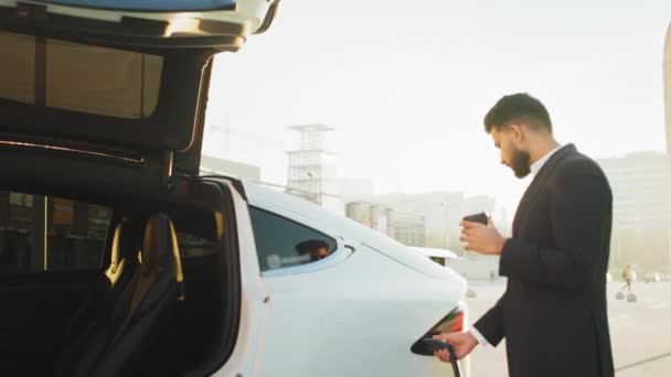 Arabski Biznesmen Garniturze Wkładający Przewód Zasilający Białego Elektrycznego Samochodu Stojąc — Wideo stockowe