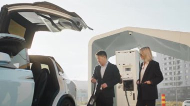 Taşıma ve satın alma konsepti. Yeni elektrikli araç alırken Asyalı bir araba satıcısıyla konuşan beyaz bir kadın. Şarj istasyonunda Moden Oto 'nun yanında duran çok ırklı insanlar. Elektrikli araba..