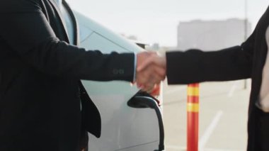 Beyaz lüks elektrikli arabanın önünde elini sıkan Kafkasyalı kadın ve Asyalı bayiye yakın çekim. İnsan kavramı, iyi bir anlaşma ve yeni ulaşım. Satıcı ve müşteri arabanın yanında el sıkışıyor.