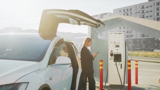 Skupiona Kobieta Biznesu Smartfonem Rękach Stojąca Pobliżu Białego Samochodu Elektrycznego — Wideo stockowe
