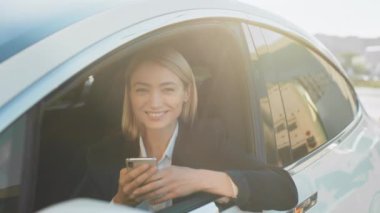 Modern akıllı telefonlu çekici beyaz kadın lüks bir arabanın içinde oturmuş aküyü şarj ediyor. Şık takım elbiseli iş kadını tatilde internette çalışıyor.