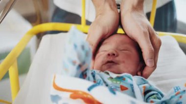 Bebek hastanenin beşiğinde, baba elini kızın kafasına koyuyor. Yeni doğmuş bir bebek ve anne babası doğum koğuşunda. Hastane beşiğinde yeni doğmuş bir bebek. Tanınmaz bir babanın el becerisi jesti korur.