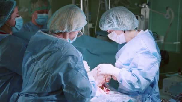 产于剖腹产 戴面具和盖帽的一组医生把头靠在病人头上 药物执行剖腹产手术 医生和护士正在拉一个新生儿 — 图库视频影像