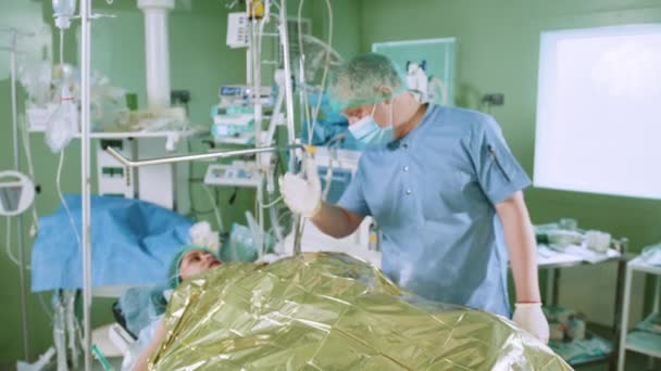 ローブとマスクのプロの成熟した外科医は 手術室で深刻な手術の前に局所麻酔の下で患者にアドバイスし 服を着ます アフリカ系アメリカ人患者と話す医師 — ストック動画