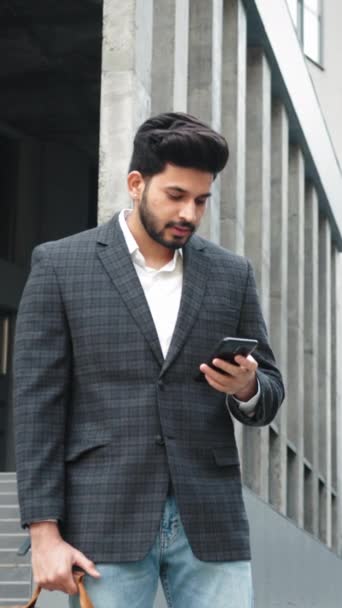 垂直屏风 穿着商务服装的时髦阿拉伯男子 站在办公中心附近 使用现代智能手机 带着手提箱在户外上网的留胡子商人 — 图库视频影像