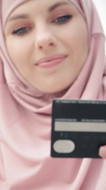 Dikey Ekran: Müslüman kadın kredi kartı ve cep telefonuyla alışveriş yapıyor. Tesettürlü çekici bir kadın ve modern akıllı telefon ve kredi kartını elinde tutan resmi kıyafetler. İnsan kavramı