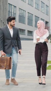 Dikey Ekran: İki Müslüman ofis çalışanı dışarıda birlikte yürüyorlar, gülümsüyorlar ve sohbet ediyorlar. Takım elbiseli yakışıklı bir adam bavul ve akıllı telefon taşıyor, tesettürlü çekici bir kadın elinde kahve tutuyor..