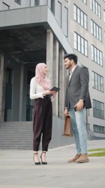 Dikey Ekran: tesettürlü çekici kadın elinde dijital tabletle müslüman meslektaşının yanında duruyor ve modern akıllı telefonu selfie çekmek için kullanıyor. İş anlayışı, insanlar ve aletler.