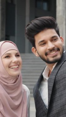 Dikey Ekran: Gülümseyen Arap iş arkadaşları şehir caddesinde dikiliyor ve modern akıllı telefondan selfie çekiyor. Tesettürlü kadın elinde dijital tabletle Müslüman meslektaşının yanında duruyor. Kavram