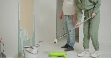 Yeni ev boyama duvarı. Ev boyanması planlayan mutlu bir çift. Neşeli çift genç adam ve kadın gülümsüyor ve yeni dairenin tadilatı sırasında kaykayla beyaz duvarı boyuyor..