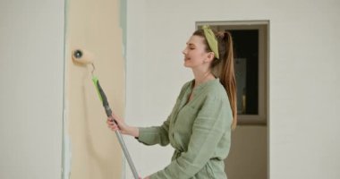 Odada onarım var. Yeni evin içinde resim yapmak. Yenileme. Kız bir odanın duvarına bigudi çiziyor. Genç, mutlu bir kadın yeni evdeki boya silindiriyle iç duvarları boyuyor. Kadın duvarı boyuyor.