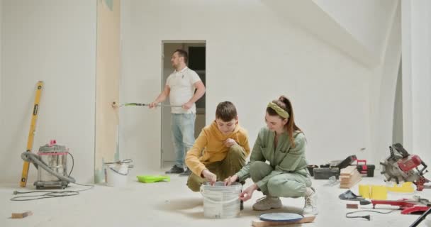 一家三口参加了一个家庭装修项目 重点是粉刷他们新公寓的内墙 爸爸用滚筒作画 妈妈和儿子在附近作画 — 图库视频影像