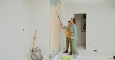 Genç bir aile yeni evlerinin duvarlarını boyayarak ev yenileme projesiyle meşgul oluyor. Anne ve oğlu birlikte çalışıyor. Etrafı boya malzemeleri ve tamamlanmamış duvarlarla çevrili. Takım çalışması.