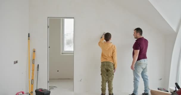 家族は新しい家の壁を描くのに忙しい 彼らは絵画用品と大きな窓でいっぱいの広々としたアパートに立っています Diyホームリフォームと家族のチームワーク — ストック動画