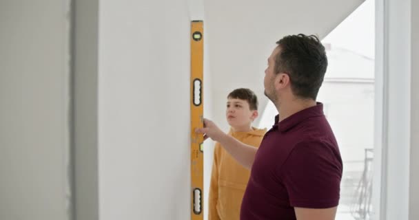 父亲和他的小儿子从事家庭装修工作 这家人积极参与修理 粉刷墙壁和测量 Diy家庭翻新项目期间的家庭联系 — 图库视频影像