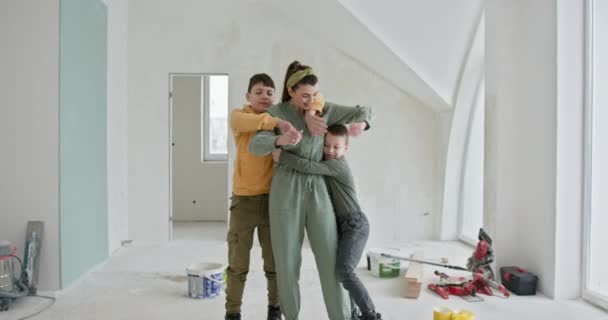一个家庭在整修房屋过程中的温馨场面 这张照片描绘了一位母亲在一间部分涂满油漆的房间里拥抱她的两个儿子 房间四周都是翻新工具和材料 — 图库视频影像