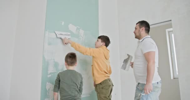 Diyホームリノベーションと壁画を一緒に楽しむ家族 家の改装プロジェクト中の家族の瞬間 父親と彼の子供たちは遊んで彼らの新しいアパートの壁を描きました — ストック動画