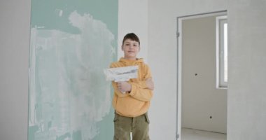 Sarı kapüşonlu ve elinde boya silindiri tutan genç bir çocuk yeni boyanmış duvarları olan bir odada gururla duruyor. Kendi kendini tamir etme ve birlikte ev dekorasyonu yapma zevki..