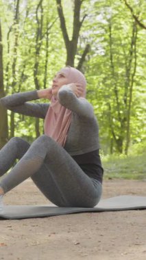 Dikey Ekran: Genç güçlü Müslüman kadın dışarıda basın pompalıyor. Spor kıyafetleri ve tesettürlü sıska bir kadın parkta kaslarını güçlendiriyor. Spor, spor, yaşam tarzı. Spor anlayışı ve sağlıklı