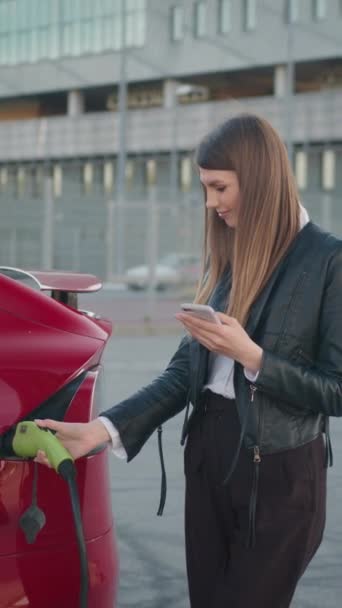 Κάθετη Οθόνη Όμορφη Γυναίκα Που Χρησιμοποιεί Smartphone Ενώ Φορτίζει Αυτοκίνητο — Αρχείο Βίντεο