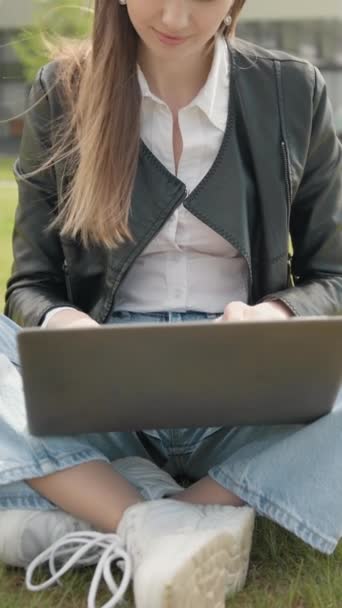 縦スクリーン 夏の公園の緑の芝生のラップトップ コンピュータで働く幸せな女性 若い女性フリーランサーは新しい注文を受け取ることを喜んでいます ノートブック屋外を利用した女子学生 ティーンエイジャー ガール — ストック動画