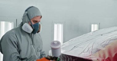 Korumalı vites spreyindeki teknisyen araba bakım istasyonundaki özel bir bölmede kırmızı araba parçası boyuyor. Araba Boyama Teknisyeni Oto Tamirhanesinde Kırmızı Boya Uyguladı.