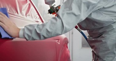 Korumalı vites spreyindeki teknisyen araba bakım istasyonundaki özel bir bölmede kırmızı araba parçası boyuyor. Araba üretim fabrikası. Otomotiv boya hizmetleri, kaliteli kaportacı konsepti.